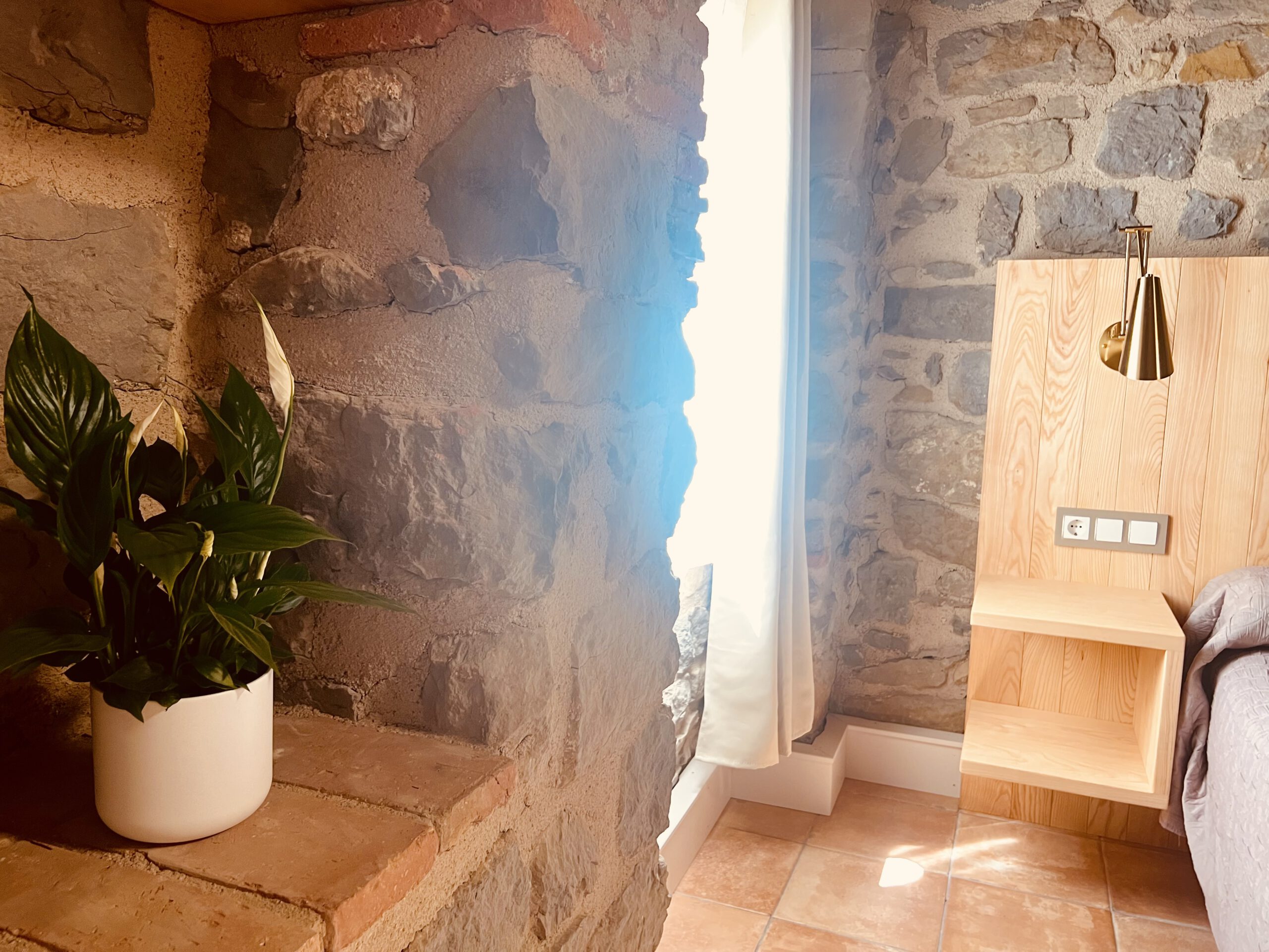 Detall de l’habitació Freixe amb paret de pedra, capçal de fusta i llum natural